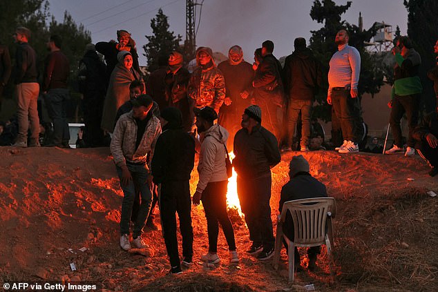 People warm themselves by the fire as they gather at Sednaya Prison in Damascus in search of loved ones