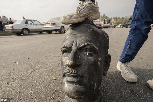 An opposition fighter steps on a broken bust of the late Syrian President Hafez Assad