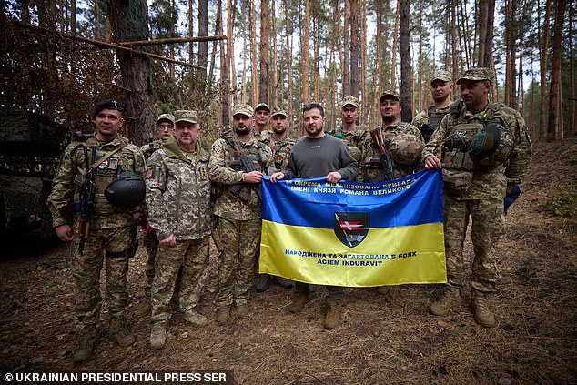 Ukrainian President Volodymyr Zelensky (C) poses for a photo with soldiers holding a Ukrainian flag. The US has sent almost $200 billion to the country in recent years