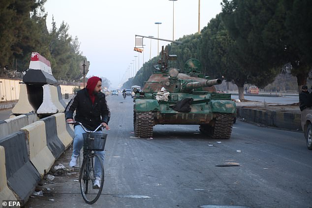 A man sits on a bicycle next to a tank in Homs, Syria, on December 8