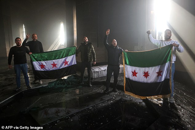 Rebel fighters stand with the Syrian flag on the burned grave of the late Syrian President Hafez al-Assad