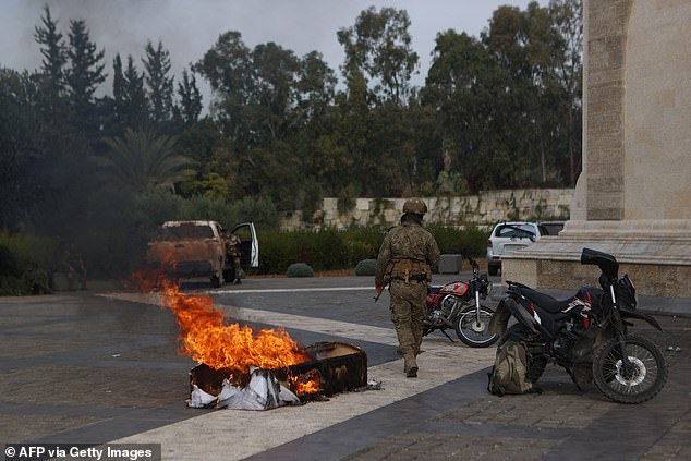 A rebel fighter walks past the burning coffin of late Syrian President Hafez al-Assad outside his mausoleum