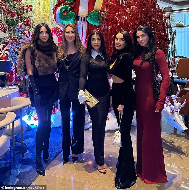 In one fell swoop, the former model showed off her enviable physique in a semi-sheer ruby ​​red dress as she posed for a photo with her glamorous friends amid lavish Christmas decorations.