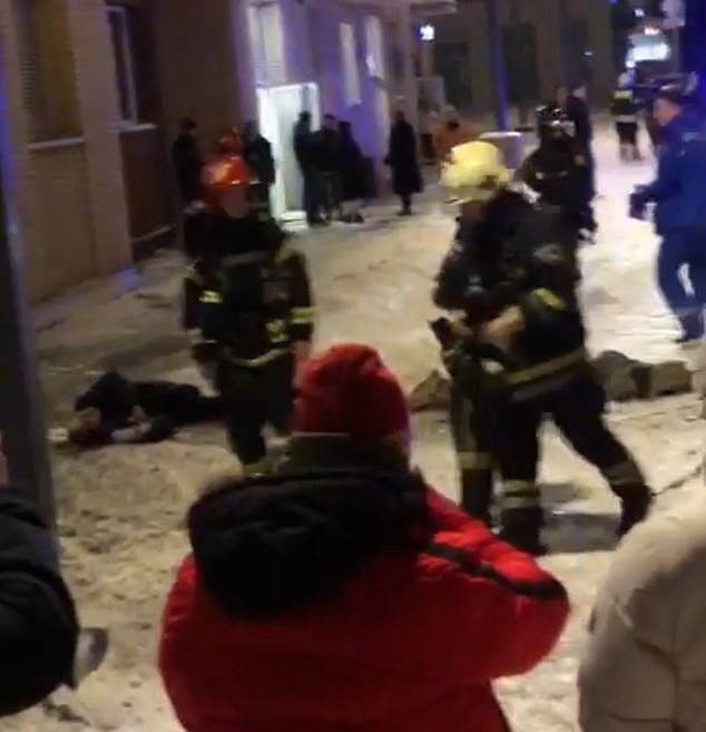 Two bodies can be seen as bystanders watch emergency services on the scene