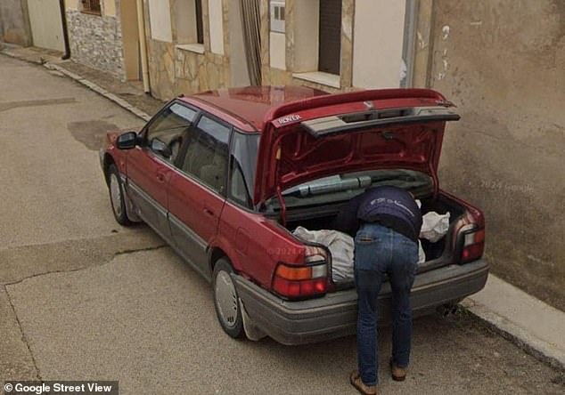 The photo shows a man loading a body bag into the trunk of a red car, local media report