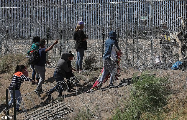 Migrants wait between barbed wire at the US border wall as they try to enter El Paso, Texas on May 26