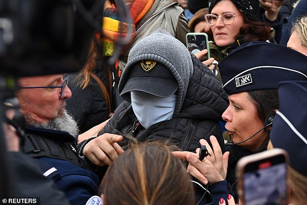 A man hiding his face is surrounded by French police, journalists and protesters as he leaves after the verdict in the trial of Dominique Pelicot