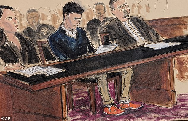 Mangione, center, sits in court Thursday reading the federal complaint while wearing orange slip-on shoes and his ankles shackled in Manhattan federal court