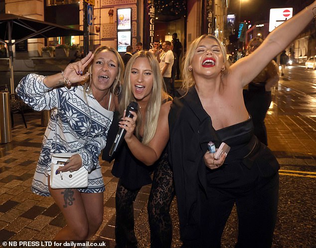 LEEDS: A blonde woman holds her karaoke microphone in the street as two friends sing along