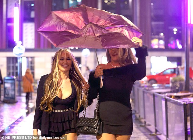 LEEDS: A woman's umbrella is blown inside out as two partygoers stand in rain-soaked streets in Leeds city center