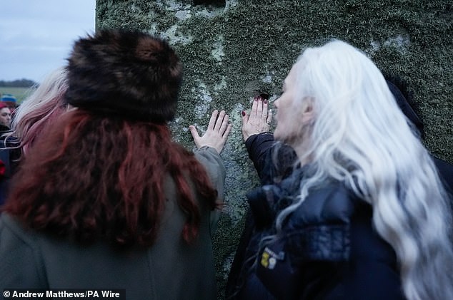 People touch one of the stones as they participate in the winter solstice celebration during sunrise at the prehistoric monument Stonehenge