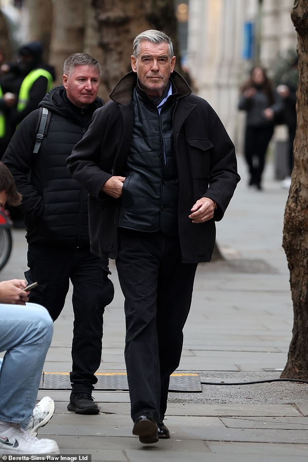 Pierce, who is clean-shaven for this project, looked dapper in a blue shirt and black pants, with a gray and brown collared trench coat over it