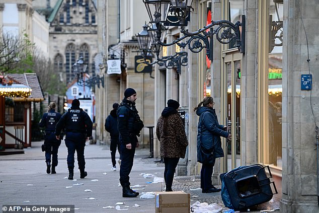 Overturned garbage bins and debris are seen as police officers walk through a closed Christmas market where a car crashed into a crowd the night before, injuring more than 60 people