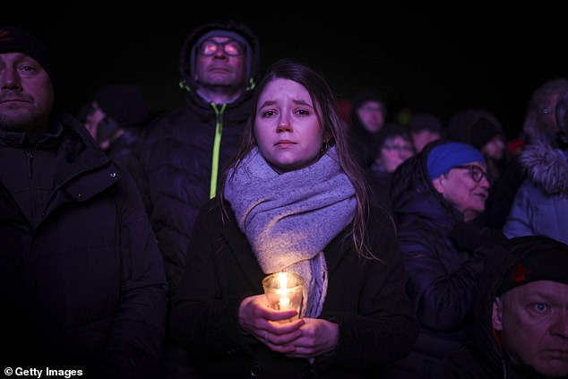 A woman holds a candle as others watch a prayer ceremony outside Magdeburg Cathedral, the day after the devastating attack