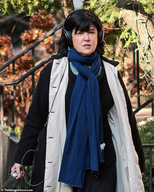 She wore a long black winter coat with beige lining over a black dress with a dark blue scarf tied at the front near her neck