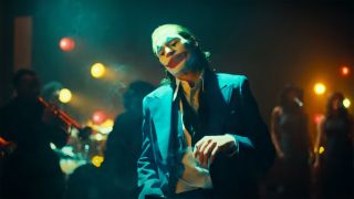 Arthur Fleck wears his signature makeup and a blue suit at a jazz club in Joker 2