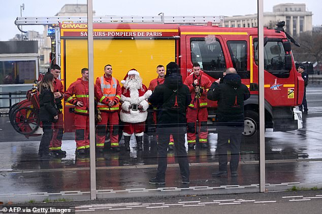 Firefighters pose for a photo with a Santa Claus at the Eiffel Tower as the site was closed and then reopened after a fire was reported in Paris on December 24