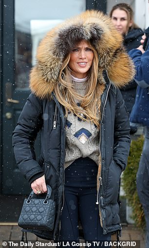 She left her cozy and chic jacket open to show off her taupe, knit sweater with navy blue details