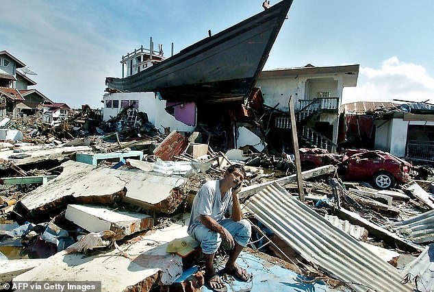 A man sits in front of a boat that was swept onto the roof of a building on December 26, 2004