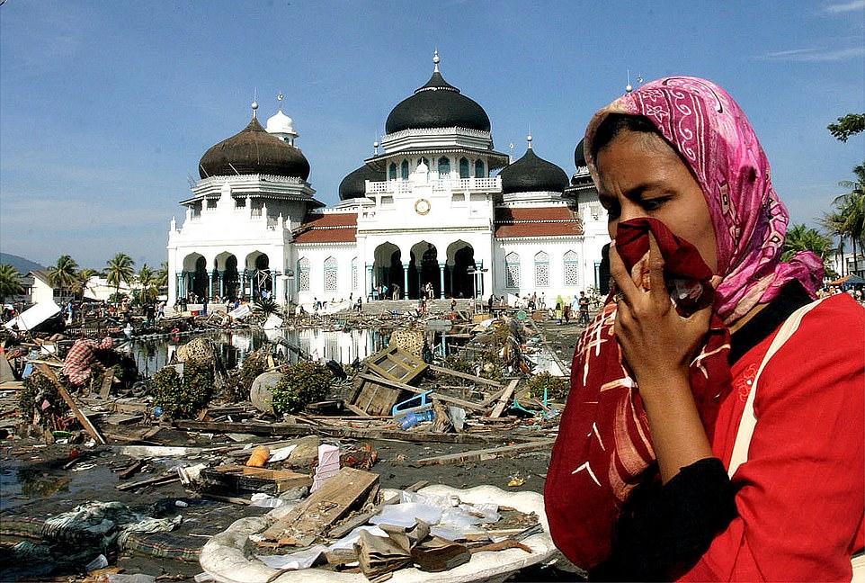 A woman walks near a mosque with the waste from the earthquake and tsunami in Banda Aceh