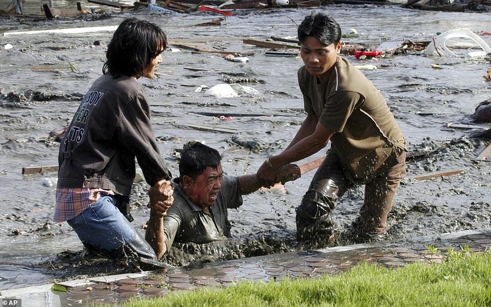 Acehnese youth try to pull a man to higher ground through a flooded street in Indonesia in the aftermath of the Boxing Day tsunami