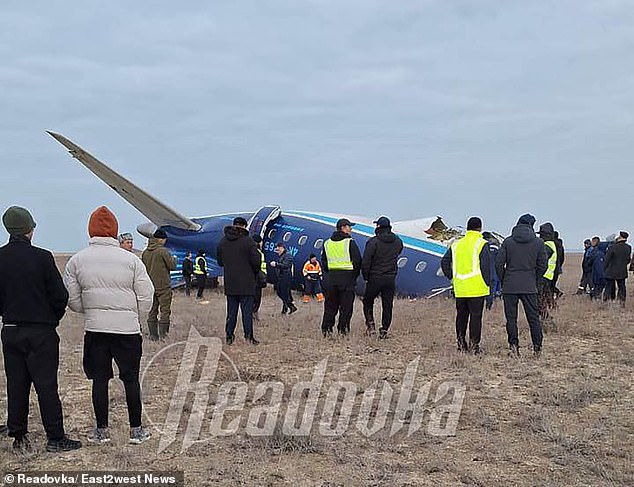 There are people standing next to the back of the crashed passenger plane