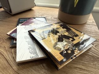 A stack of CDs on a desk. A loudspeaker and a plant can be seen in the background.