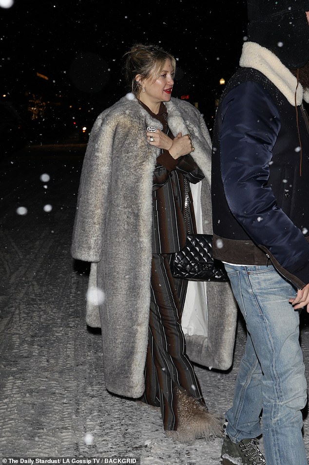 She modeled an elegant fur coat on top of a brown and gray striped blazer and matching pants as she walked through the piled snow