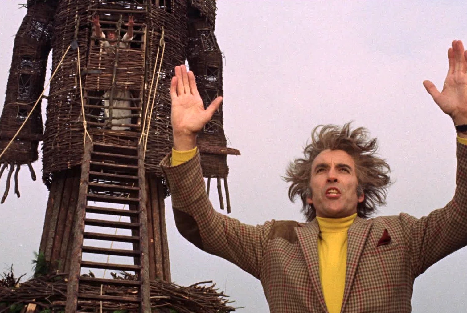 Lord Summerisle holds two hands in the air as he preaches to the crowd and the wicker man and Sgt. Neil Howie on fire