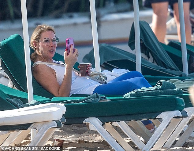 Before going for a dip, Claire cut a casual figure in a white cardigan and blue leggings as she relaxed on a beach chair with a cup of coffee.