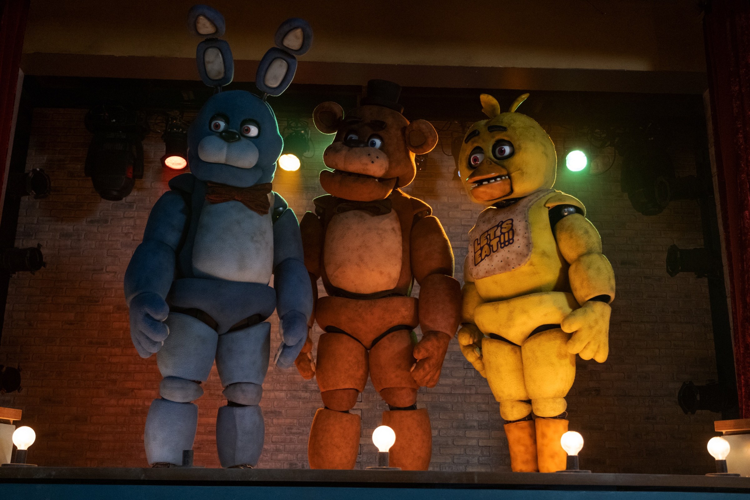 Animatronics Bonnie, Freddy Fazbear, and Chica stand on a stage, looking right, in the Universal Pictures film adaptation Five Nights at Freddy's