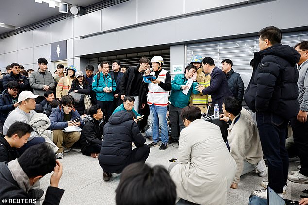 People listen at Muan International Airport as an official announces the additional names of passengers who died in the horror plane crash