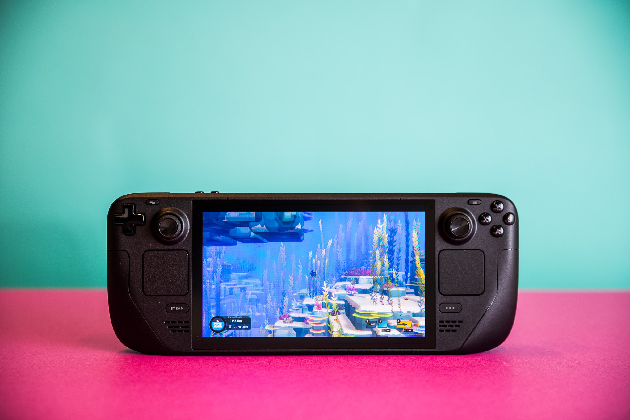 Photos of the Steam Deck OLED and of the zippered hard case. Each photo is taken while the handheld sits on a bright pink sheet of thick paper.