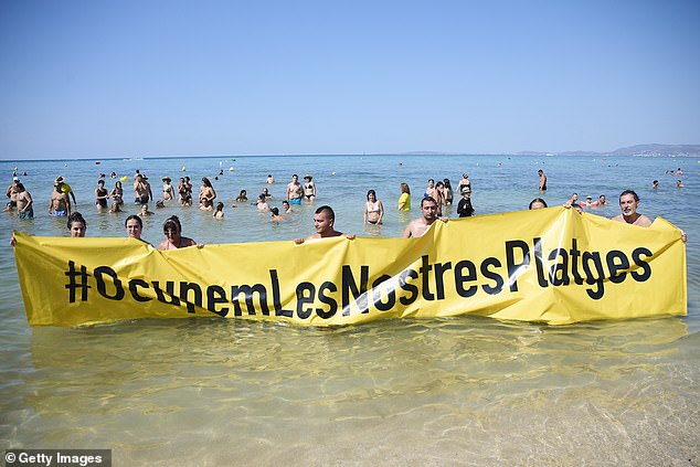 Members of the Mallorca Platja Tour association demonstrate against tourist saturation with a banner reading 'Let's occupy our beaches!' on the beach of Palma de Mallorca on August 11, 2024 in Mallorca, Spain