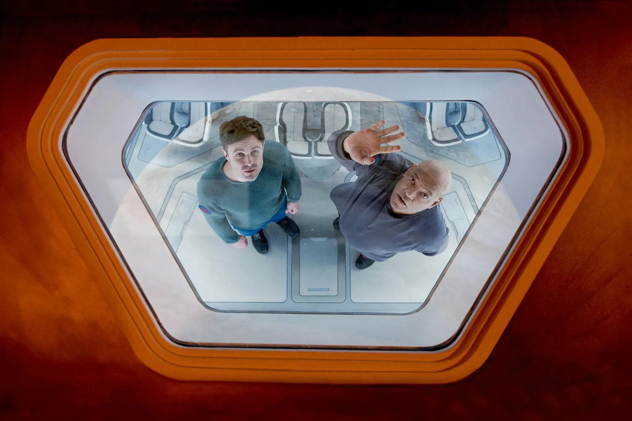 Casey Affleck and Laurence Fishburne stare through the porthole of a spaceship in Slingshot