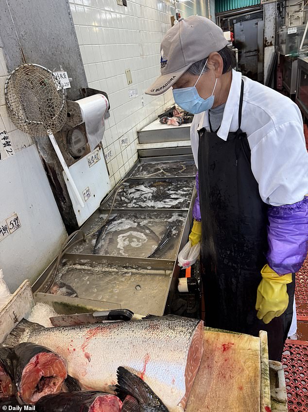 Bloody fish carcasses lay atop unclean green and brown discolored cutting boards - next to their remains, live fish lay gasping for breath in small pools filled with four inches of water