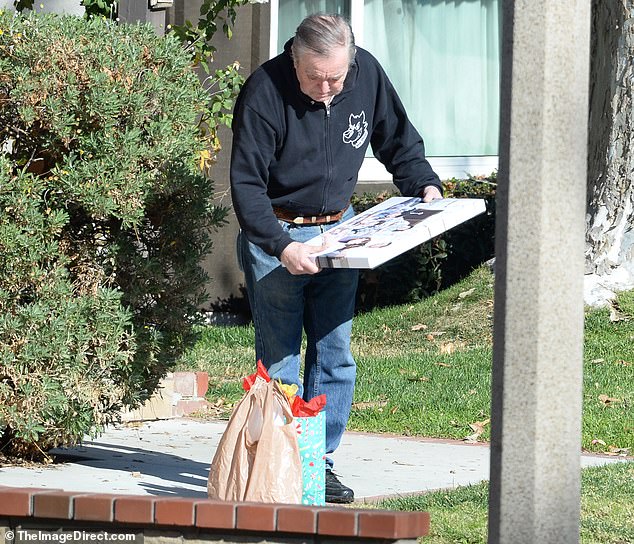 He wore a black top with belted jeans while holding a photo of the Leave it To Beaver cast