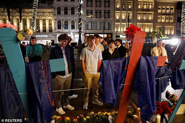 A group of friends mourn the loss of Hubert Gauthreaux whose photo is placed on a wooden cross, among others who died