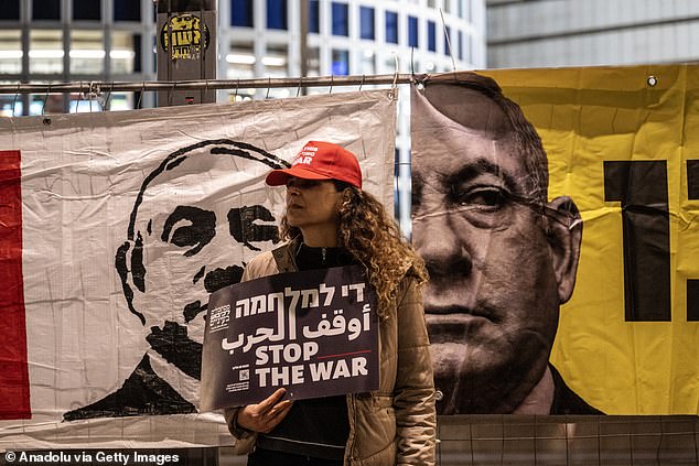 An anti-war protester wearing a 'Make America Great Again' hat stands in front of anti-Netanyahu banners