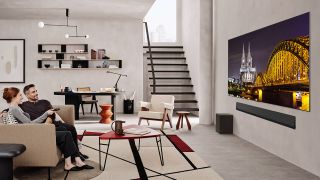 Two people are watching the LG G5 TV, which hangs on the wall in a spacious living room