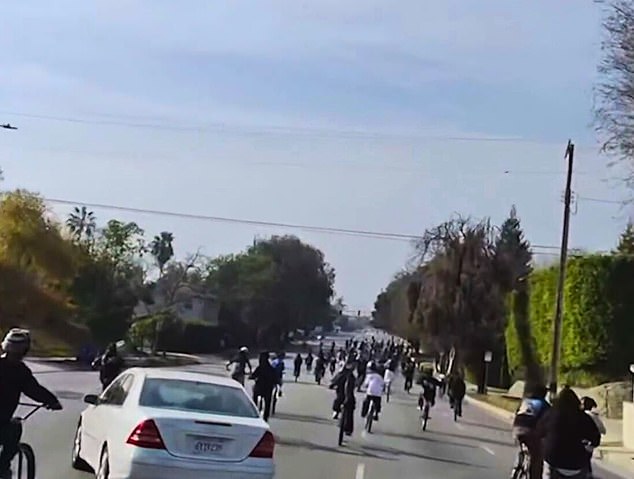 The white car swerved into oncoming traffic, narrowly avoiding the crowd of cyclists