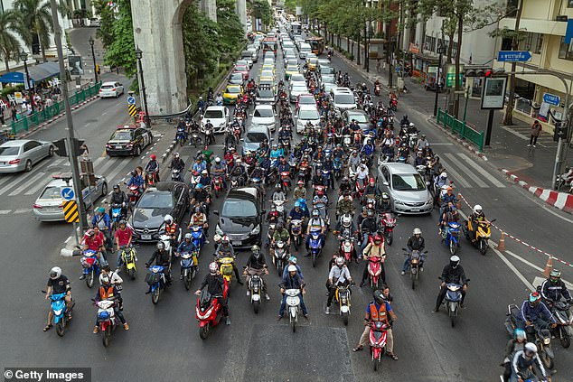 Several scooters and cars wait at traffic lights on Ratchadamri Road in Bangkok, Thailand