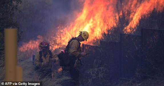 Firefighters are working to extinguish a fire that raged near homes in Pacific Palisades, California on January 7, 2025. A fast-moving wildfire in a Los Angeles suburb burned buildings and prompted evacuations Tuesday. "life-threatening" winds whipped the region. More than 200 acres burned in Pacific Palisades, a luxury spot of multi-million dollar homes in the Santa Monica Mountains, shutting down a major highway and blanketing the area in thick smoke. (Photo by David Swanson/AFP) (Photo by DAVID SWANSON/AFP via Getty Images)