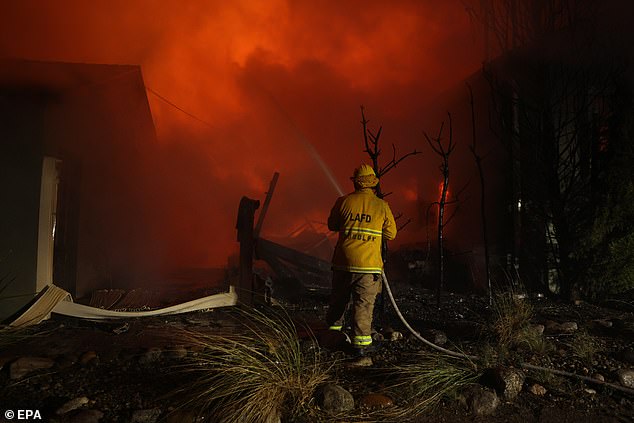 A firefighter hoses down a burning house after the Palisades wildfire in Los Angeles