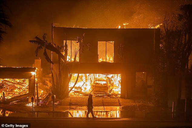 A firefighter watches the flames from the Palisades Fire, burning homes on Pacific Coast Highway