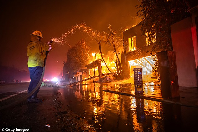 A firefighter battles the Palisades Fire as homes are torched on Pacific Coast Highway during a powerful storm on January 8