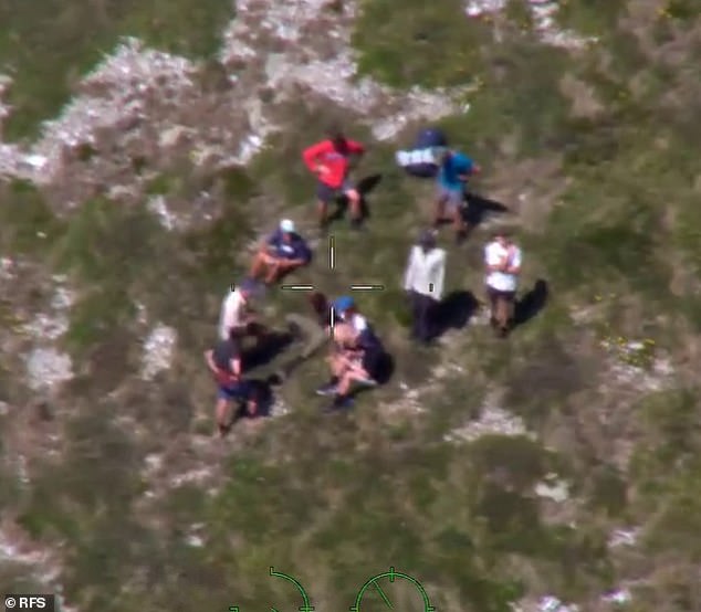 Mr Nazari (pictured sitting with the hikers) was found after noticing a group of passing hikers and calling out to them, explaining that he was lost and thirsty