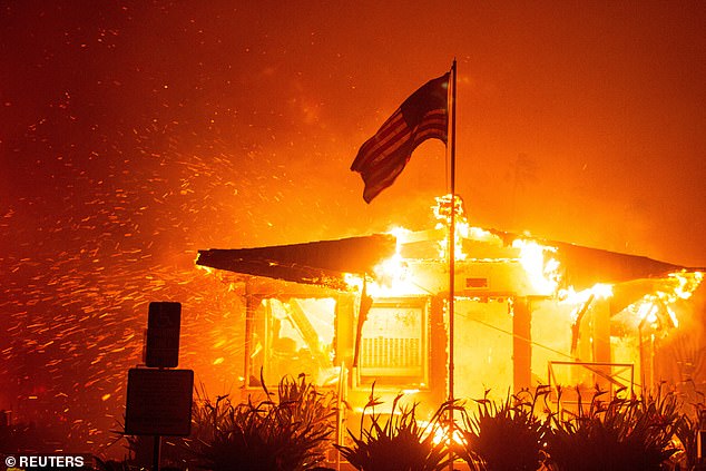 The American flag flies as fire engulfs a building as the Palisades Fire burns during a storm