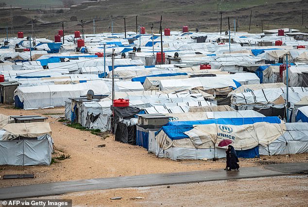 Women use an umbrella as they walk through the rain in 2021 at Roj camp, where relatives of people suspected of joining the Islamic State are being held