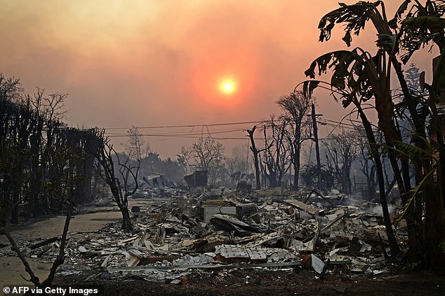 The sun can be seen behind smoke above charred buildings amid the Palisades Fire yesterday